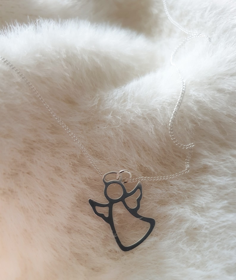 May include: A silver chain necklace with a delicate angel pendant. The angel is outlined in silver and has a halo.