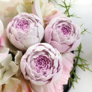 May include: A bouquet of artificial flowers in a black vase. The bouquet features three large, white peonies with pink centres, surrounded by smaller white and pink roses.