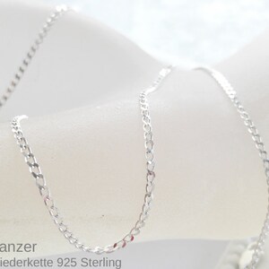 May include: A silver chain necklace with a curb link style. The chain is on a white surface. Panzer Gliederkette 925 Sterling.