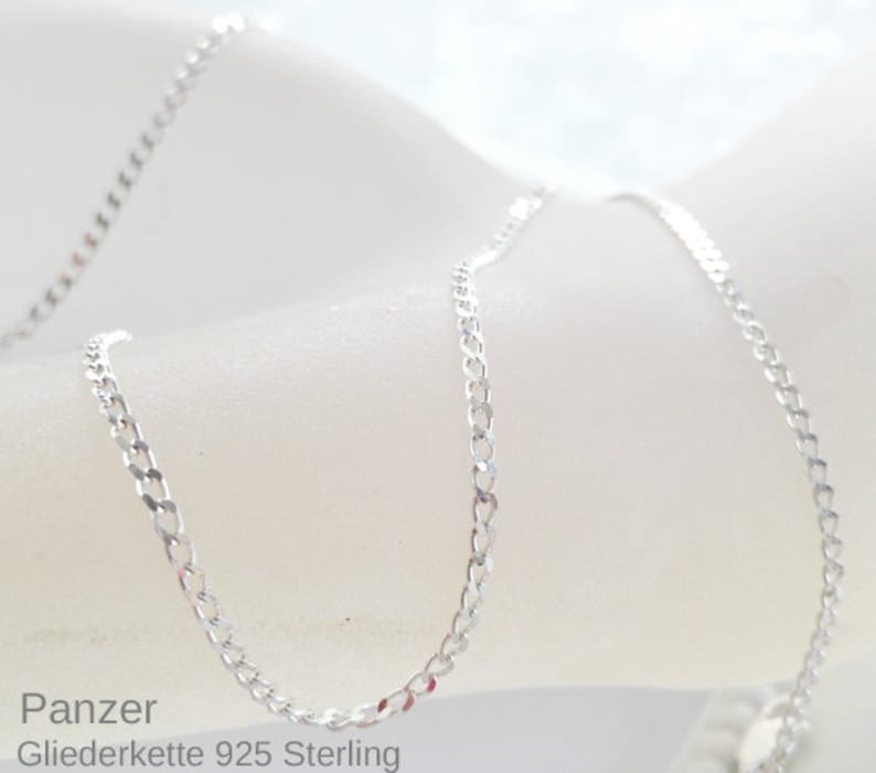 May include: A silver chain necklace with a curb link style. The chain is on a white surface. Panzer Gliederkette 925 Sterling.