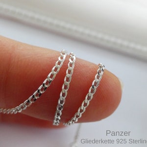 May include: A silver chain necklace with a curb link style. The chain is shown coiled on a finger. The text "Panzer Gliederkette 925 Sterling" is visible in the image.