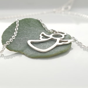 May include: A silver chain necklace with a delicate angel pendant. The pendant is a cutout design of an angel with wings outstretched.
