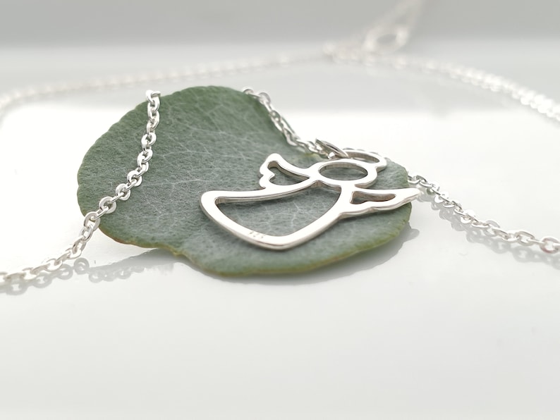 May include: A silver chain necklace with a delicate angel pendant. The pendant is a cutout design of an angel with wings outstretched.