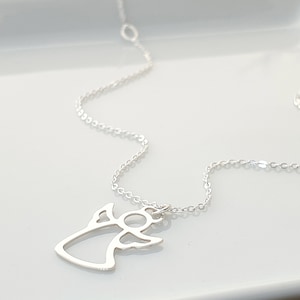 May include: A silver chain necklace with a delicate angel pendant. The angel is cut out in a simple, minimalist style.