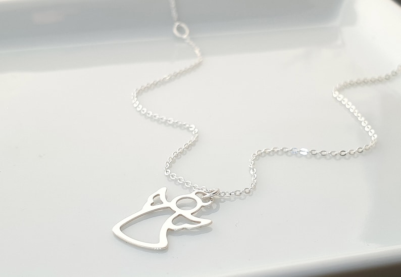 May include: A silver chain necklace with a delicate angel pendant. The angel is cut out in a simple, minimalist style.
