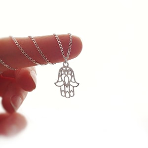 Può includere: Una collana a catena d'argento con un ciondolo a forma di mano di Hamsa. La mano di Hamsa è un simbolo popolare di protezione e buona fortuna.