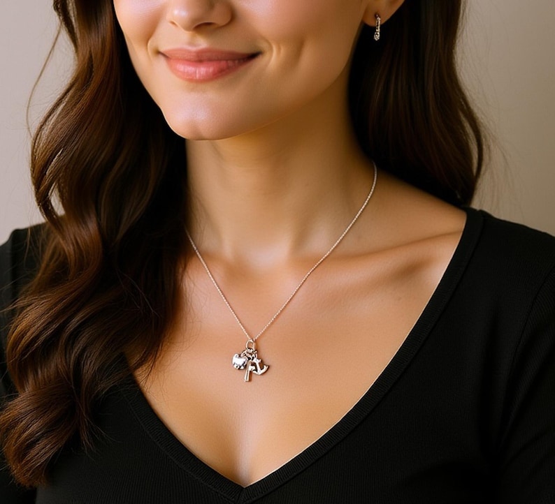 May include: A silver necklace with three charms: a heart, an anchor, and a key. The necklace is worn against a black top. The charms are small and detailed, with a shiny finish. The necklace is a delicate piece of jewelry.