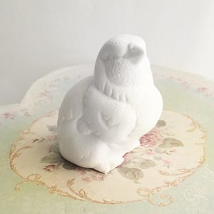 Puede incluir: Escultura de cerámica blanca de dos pájaros, uno posado sobre el otro. Los pájaros son estilizados y tienen un diseño simple y moderno.