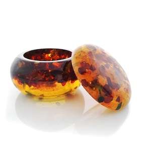 Op de afbeelding: Een ronde amberen sieradenbox met een deksel. De doos en het deksel zijn gemaakt van amber met insluitsels in verschillende kleuren, waaronder rood, geel en groen.
