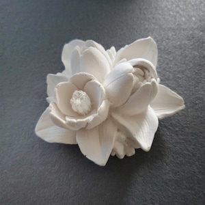 May include: A white ceramic flower sculpture with multiple petals and a detailed center. The sculpture is a decorative piece for a home or office.