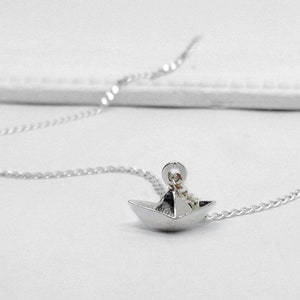 May include: A silver chain necklace with a small, origami paper boat pendant.
