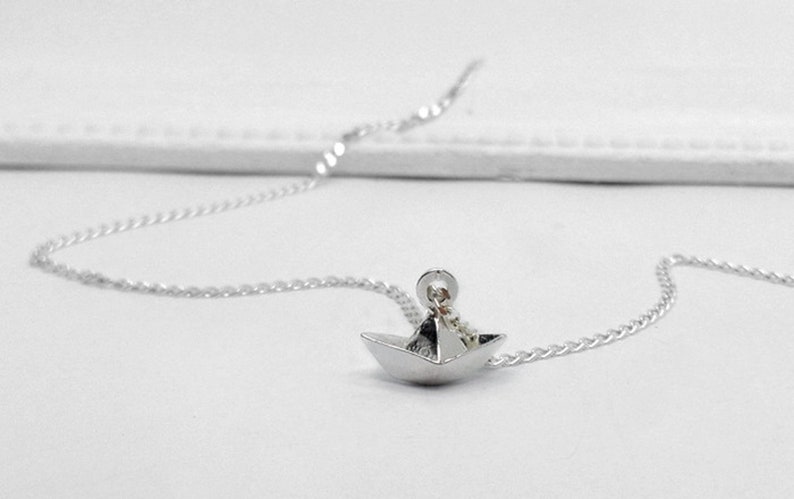 May include: A silver chain necklace with a small, origami paper boat pendant.
