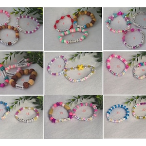 May include: A collection of twenty-two colourful beaded bracelets arranged in a grid, featuring various combinations of plastic, wooden, and lettered beads. Each bracelet is numbered and displays unique patterns, colour schemes, and words.