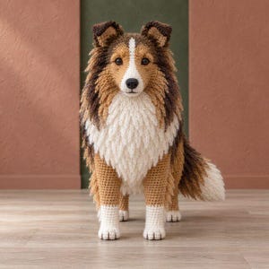 Può includere: Un animale di peluche all'uncinetto a forma di cane pastore delle Shetland. Il cane presenta un mantello tricolore in filato color marrone chiaro, marrone scuro e bianco. Ha il petto bianco, le zampe bianche e una striscia bianca sul muso.