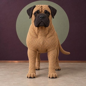 May include: A handcrafted crochet dog figurine featuring a tan body with a dark brown muzzle, ears, and paw details. The textured yarn construction creates a realistic appearance of a mastiff-type canine standing in a forward-facing position.