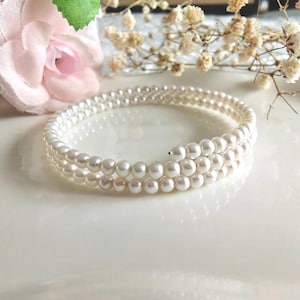 May include: A multi-strand wrap bracelet featuring small, round, white pearls arranged in a continuous spiral design. The bracelet consists of three overlapping loops of uniform, lustrous white beads that create a layered appearance.