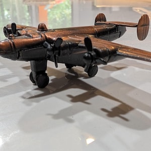 Op de afbeelding: Een metalen modelvliegtuig in bronskleur met een dubbel staartstuk, vier propellers en een landingsgestel. Het vliegtuig heeft een gedetailleerde romp met een cockpitraam en motorgondels gemonteerd op de vleugels in een statische pose.