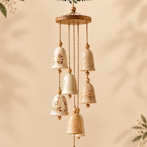 May include: A hanging mobile featuring five speckled ceramic bells and a leaf-shaped pendant suspended from a circular wooden top by twisted cords. The bells are decorated with brown botanical illustrations. Text reads Hanging Bells Template.