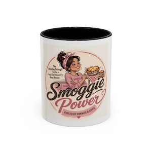 May include: A white ceramic mug with a black interior and rim, featuring a graphic of a person wearing a pink shirt and headband. The text reads Smoggie Power, Fueled by Parmos & Chips, and The Middlesbrough Taste. Real Community. Real Power.
