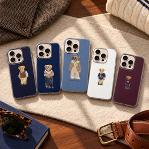May include: Five smartphone cases featuring a Ralph Lauren bear graphic. The cases come in navy, light blue, white, and dark maroon colors. Each case displays a different bear illustration wearing various outfits, including sweaters and vests.