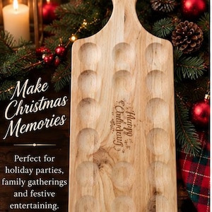 May include: A light-colored wooden serving board with a handle and fifteen circular indentations arranged in three columns. The board features the engraved text "Happy Christmas" in a decorative script font on its surface.
