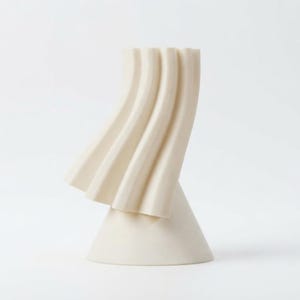 May include: A cream-colored sculptural object featuring a smooth, conical base that transitions into a series of vertical, undulating, wave-like ridges that curve outward and upward, creating a distinct, asymmetrical, and textured silhouette.