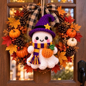 May include: A crochet ghost ornament wearing a purple witch hat with a yellow star and a yellow and purple striped scarf, holding a small orange pumpkin. The ghost is centered on a wreath decorated with pinecones, orange pumpkins, and autumn leaves.