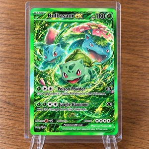 Könnte beinhalten: Eine Bulbasaur ex Sammelkarte mit 180 KP, in einer transparenten Kunststoff-Schutzhülle. Die Karte zeigt grüne Illustrationen von Bulbasaur und Venusaur sowie Text zu den Attacken Poison Powder und Jungle Hammer und der Pokémon ex-Regel.