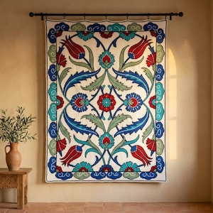 May include: A rectangular wall hanging featuring a symmetrical floral pattern with red tulips, blue and green leaves, and a central red flower. The design is enclosed by a decorative border of blue and white scalloped shapes on a cream background.