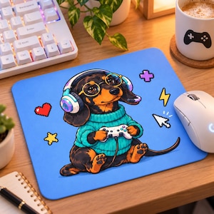 May include: A rectangular light blue mousepad featuring a black and tan dachshund wearing a teal sweater, round glasses, and gaming headphones while holding a white game controller, surrounded by pixelated icons of a heart, star, cross, and lightning bolt.