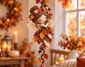 May include: A crocheted fairy doll with brown hair adorned with small flowers, wearing a skirt made of layered autumn-colored leaves. The figure has cream-colored wings and is suspended by a vine featuring acorns and a red-and-white spotted mushroom.