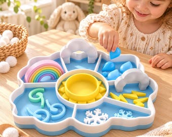May include: A cloud-shaped sorting tray with a central yellow sun, featuring compartments containing a rainbow, blue raindrops, yellow lightning bolts, white snowflakes, and light blue letter shapes, all made of smooth plastic material.