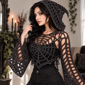 Puede incluir: Un top de ganchillo gris oscuro con capucha que presenta un patrón de telaraña calado en el pecho y mangas largas acampanadas. La prenda se lleva sobre una camiseta de tirantes negra y se combina con vaqueros negros, creando un look.