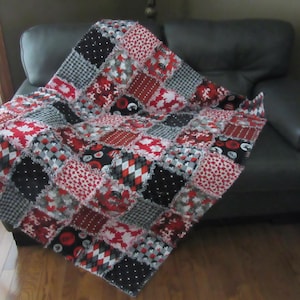 Peut inclure: Une courtepointe patchwork faite à la main, rouge, noire, blanche et grise. Elle présente divers motifs, dont des pois, des carreaux et des motifs floraux. La courtepointe est drapée sur un canapé gris foncé, mettant en valeur ses couleurs et textures.