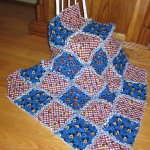 May include: A blue and red patchwork quilt with a Mickey Mouse print. The quilt is made of squares of different fabrics and has a ruffled edge.