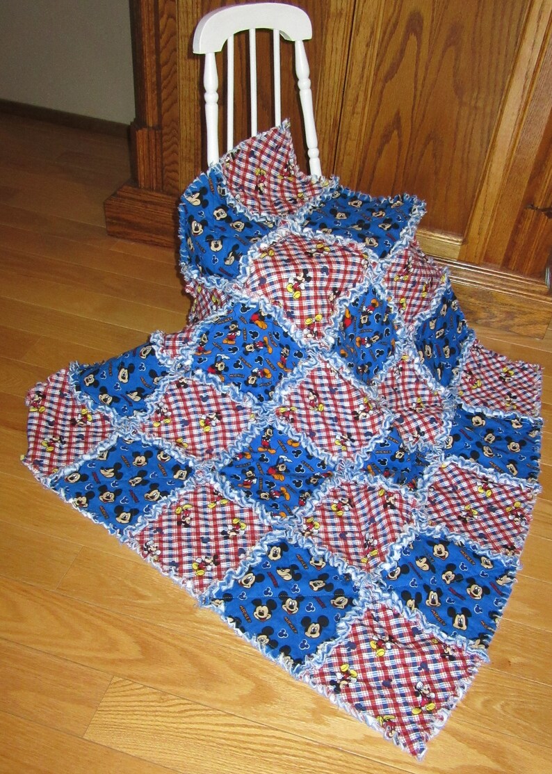 May include: A blue and red patchwork quilt with a Mickey Mouse print. The quilt is made of squares of different fabrics and has a ruffled edge.