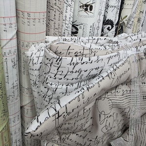 May include: A collection of fabric bolts featuring various printed designs including black cursive handwriting on a beige background, red and black grid ledger patterns, and black and white illustrations of insects and postage stamps.