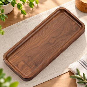 May include: A rectangular wooden serving tray with rounded corners and a smooth, polished finish. The tray features a deep brown color with visible natural wood grain patterns throughout the flat surface and raised edges.