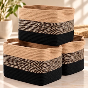 May include: A set of three rectangular storage baskets crafted from coiled rope. Each basket features a two-tone design with a natural tan upper section and a solid black base, separated by a textured, woven band of alternating black and tan rope.
