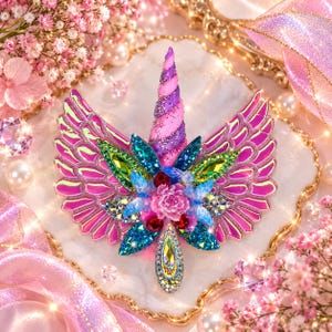Könnte beinhalten: Ein dekoratives Einhorn-Emblem mit einem gedrehten rosa-violetten Horn, irisierenden rosa Flügeln und einer zentralen Anordnung aus leuchtend grünen, blauen und roten facettierten Kristallen. Das Design ist mit kleinen floralen Akzenten verziert.