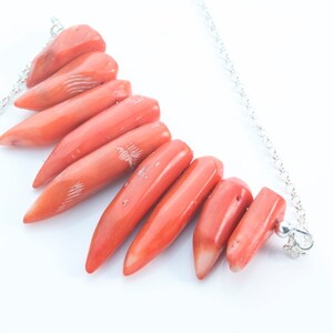 May include: A silver chain necklace with a cluster of coral-colored, pointed, teardrop-shaped beads.