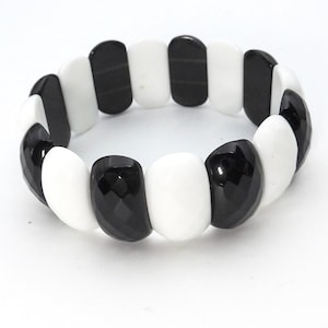 Op de afbeelding: Een zwart-witte stretcharmband. De armband heeft afwisselend zwarte en witte rechthoekige kralen. De kralen hebben een facet, licht afgeronde vorm. De armband wordt op een witte achtergrond getoond.