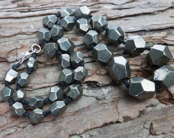 May include: A necklace made of faceted pyrite beads strung on black cord. The beads are a dark gray color and have a metallic sheen.