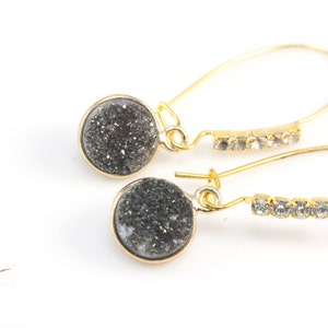 May include: A pair of gold dangle earrings with black glitter round stones and clear rhinestone accents.