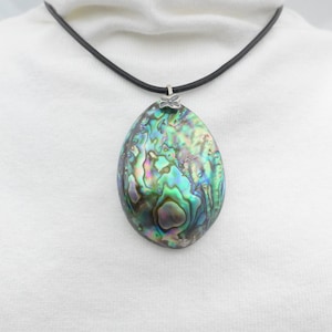 May include: A pendant necklace featuring a large, oval-shaped abalone shell with iridescent swirls of green, blue, and purple. The shell is attached to a simple black cord by a small silver-toned metal bail with a butterfly-shaped detail.