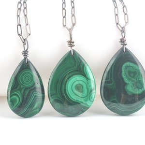Puede incluir: Tres collares de cadena plateada con colgantes de malaquita verde en forma de lágrima. Cada colgante tiene un patrón único de remolino.