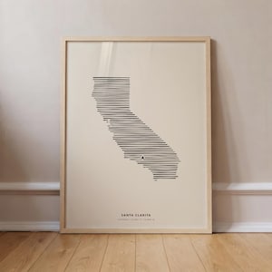 Può includere: Una stampa artistica incorniciata con una mappa della California a linee nere su sfondo crema. La mappa è composta da linee orizzontali nere con una piccola stella che segna Santa Clarita. Il testo riporta SANTA CLARITA CALIFORNIA 34.4208 N 118.5358 W.