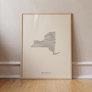 Puede incluir: Una lámina enmarcada con un mapa de líneas negras del estado de Nueva York compuesto por rayas horizontales sobre fondo crema. El texto NEW ROCHELLE y las coordenadas están impresos en negro en la parte inferior del marco de madera clara.