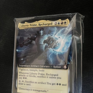 May include: A Liberty Prime, Recharged trading card encased in a clear plastic sleeve. The card features a metallic robot illustration with blue electrical energy, text detailing its abilities, an 8/8 power and toughness, and the quote Democracy is nonnegotiable.