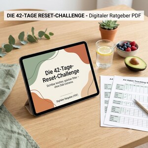 Könnte beinhalten: Ein Tablet mit einem digitalen Ratgeber namens Die 42-Tage Reset-Challenge und abstrakten Formen in Salbeigrün, Terrakotta und Creme. Daneben liegen A4-Gewohnheitstracker, ein Glas Wasser mit Zitrone und eine halbierte Avocado.